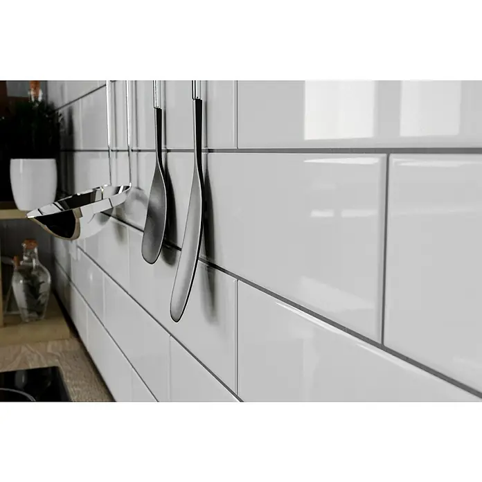 Modern Style Wandfliese Urban Blanco - 7,5 x 30 cm, Weiß, Glänzend - Nahaufnahme einer Küchenrückwand mit weißen Fliesen und daran hängenden Küchenutensilien, die eine moderne und saubere Ästhetik zeigen.