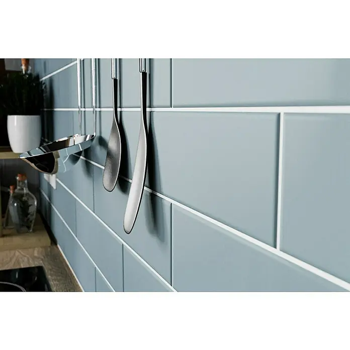 Modern Style Wandfliese Urban Oceano - 7,5 x 30 cm, Blau, Matt - Nahaufnahme einer hellblauen Küchenrückwand mit weißen Fugen und hängenden Küchenutensilien aus Edelstahl, die eine moderne Ästhetik verleihen.