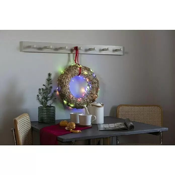 Konstsmide LED-Lichterkette Bunt - Lichtfarbe: Mehrfarbig, Anzahl Leuchtmittel: 35 Stk., Netzbetrieben, IP20 - Strohkranz mit bunten Lichtern, hängt an einer weißen Garderobe über einem festlichen Tischarrangement.