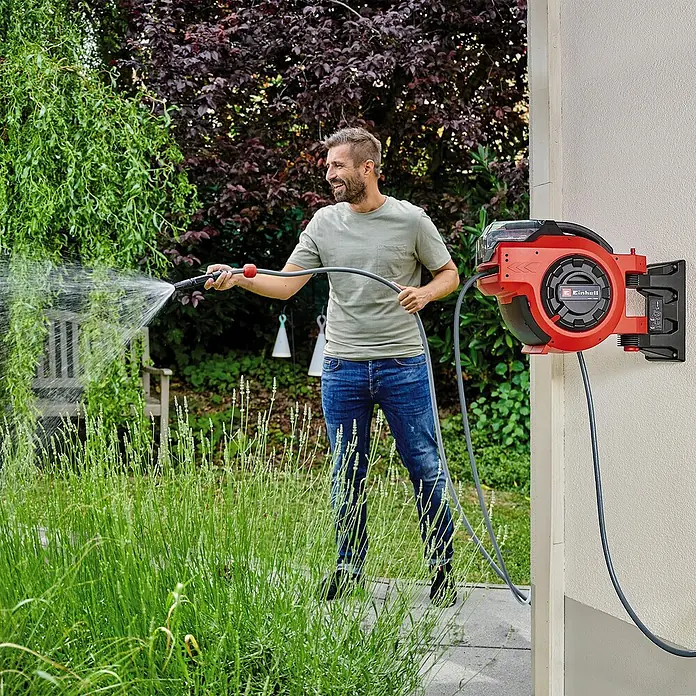Einhell Power X-Change 18V Akku-Schlauchtrommel GE-HR 18/30 - 18 V, Ohne Akku - Ein Mann benutzt eine Einhell Wand-Schlauchbox zum Bewässern des Gartens. Die Box ist rot und schwarz und an einer Wand befestigt.