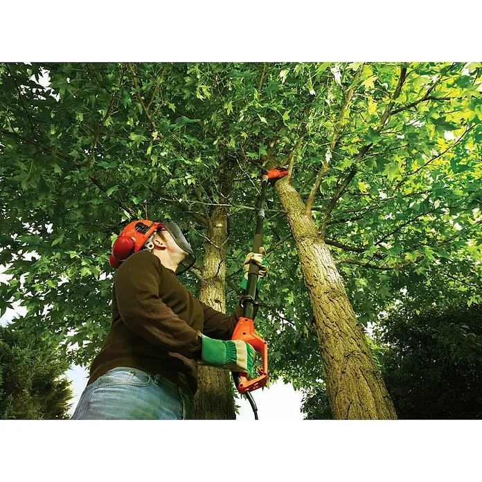 Black+Decker Podadora eléctrica PS7525-QS - 800 W - Un hombre usa una motosierra de pértiga para recortar ramas en un árbol, equipado con equipo de seguridad para un trabajo seguro al aire libre.