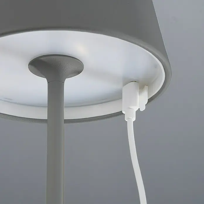 FHL easy Akku-Tischleuchte COSENZA - 2 W, L x B x H: 12 x 12 x 38 cm, Sand, RGB, 1 Stk. - Nahaufnahme einer modernen grauen Lampe mit weißem Lampenschirm und weißem Kabel, das eingesteckt ist.
