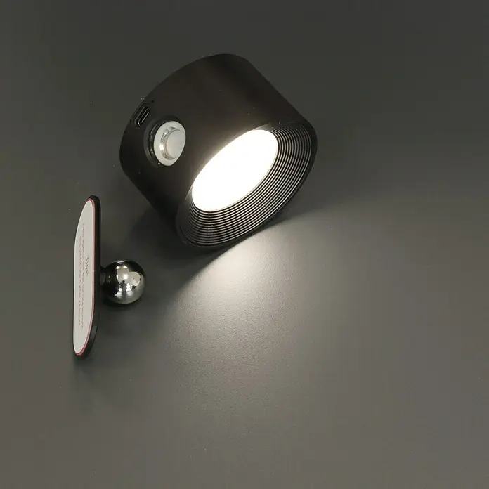 FHL easy Magnetic Akku-Wandleuchte - 9,5 x 8 x 4,5 cm, Schwarz, Mehrfarbig, 2 W, IP20 - Nahaufnahme einer schwarzen, magnetischen LED-Leuchte mit einem Knopf zur Steuerung auf einer grauen Oberfläche.