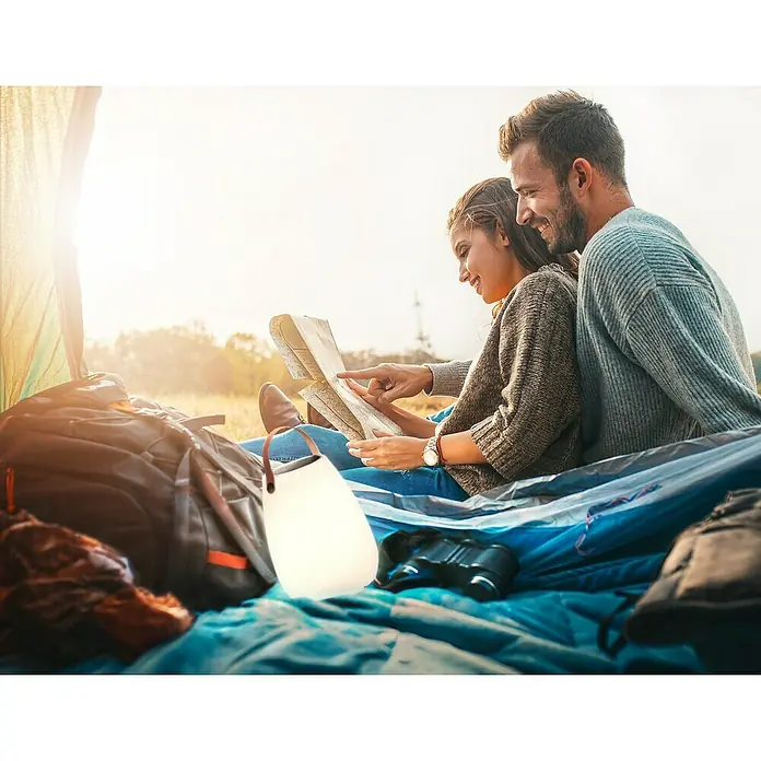FHL easy Akku-Tischleuchte RUBY Solar - 0,5 W, L x B x H: 18 x 18 x 30 cm, Weiß, RGB - Ein Paar sitzt im Zelt und plant seine Route mit einer Karte, während eine sanfte Lampe für warmes Licht sorgt.