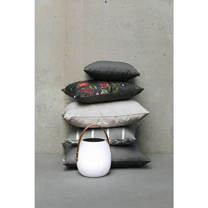 SCHÖNER WOHNEN-Kollektion Akku-Tischleuchte BELL - 2 W, L x B x H: 22 x 22 x 34 cm, Weiß, RGB - Ein Stapel dekorativer Kissen mit einer tragbaren Lampe davor, vor einer grauen Wand.