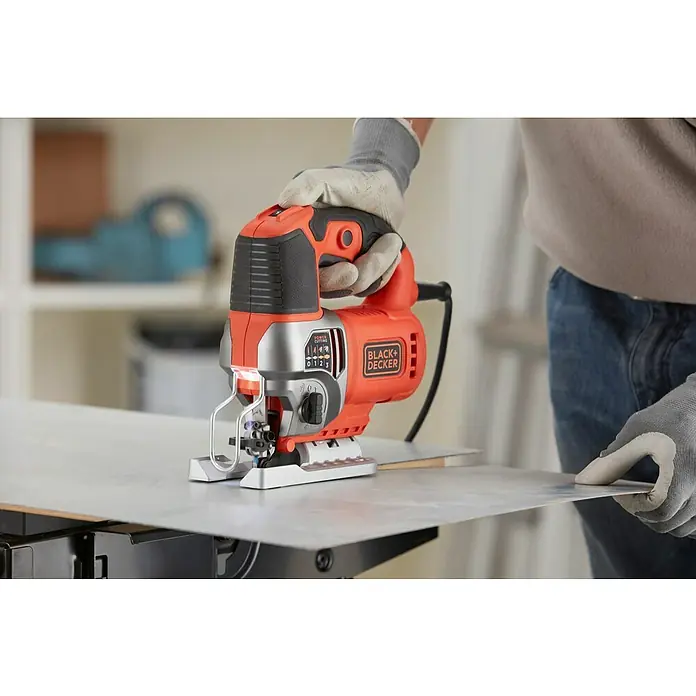 Black+Decker Sierra de calar eléctrica BES610KA5 - 1.000 /min - 3.100 /min, 90 mm - Primer plano de una sierra de calar Black+Decker en acción, cortando una pieza de metal, operada por una persona con guantes.