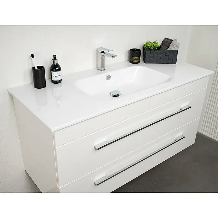 Lanzet K5 Badmöbel-Set K51W2 - 117,9 cm, Weiß - Modernes, weißes Badezimmerwaschbecken mit zwei Schubladen und verchromten Griffen, darauf Seife, Zahnbürste und Dekoration.