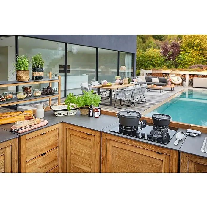 Sunfun Zoe Outdoorküchen-Modul Kochfeld - Braun, B x T x H: 80 x 63 x 96,7 cm, Teakholz - Draufsicht auf eine Outdoor-Küche mit Holzelementen, Kochfeld, Töpfen und diversen Lebensmitteln neben einem Pool mit Gartenmöbeln.