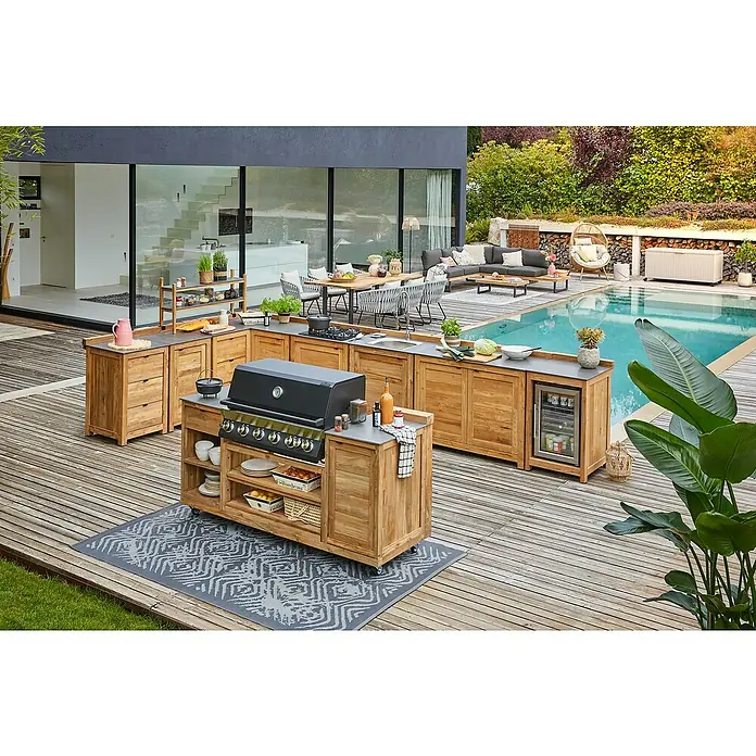 Sunfun Zoe Outdoorküchen-Modul Grillinsel - Braun, B x T x H: 188 x 67 x 96,7 cm, Teakholz - Eine luxuriöse Outdoor-Küche mit Grill, Spüle und Kühlschrank, eingebettet in eine idyllische Gartenszene am Pool.