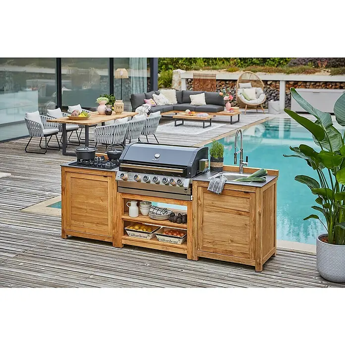 Sunfun Zoe Outdoorküchen-Modul Kochfeld - Braun, B x T x H: 80 x 63 x 96,7 cm, Teakholz - Outdoor-Küche mit Grill und Spüle auf einer Holzterrasse neben einem Pool. Die Küche ist mit Holzschränken und Regalen ausgestattet.