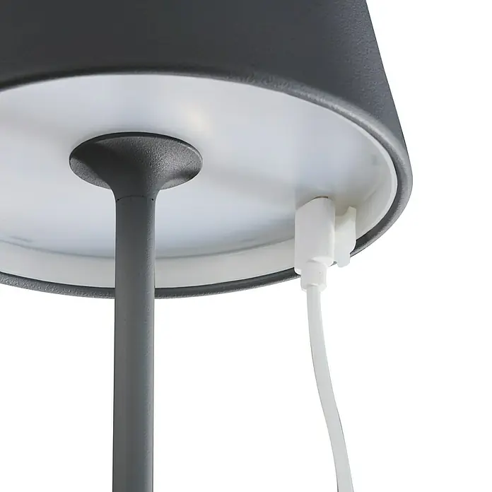 FHL easy Akku-Tischleuchte COSENZA 2.0 - 2 W, L x B x H: 11 x 11 x 34 cm, Sandschwarz, RGB - Nahaufnahme einer stilvollen Tischleuchte mit grauem Lampenschirm und einem weißen USB-Ladekabel, das an die Lampe angeschlossen ist.