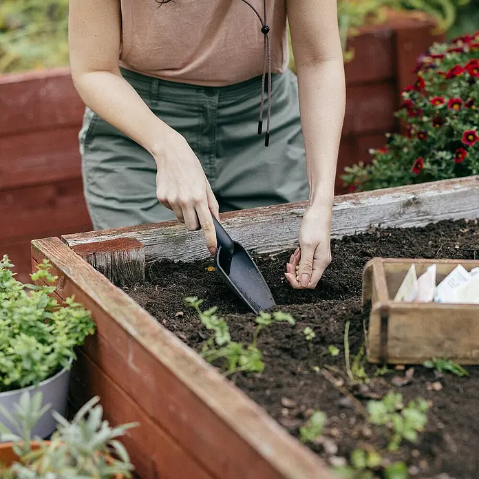 Fiskars Solid Blumenkelle - 28,2 cm - Eine Person pflanzt mit einer kleinen Schaufel Samen in einem Hochbeet. Die Schaufel ist ein großartiges Werkzeug für die Gartenarbeit.