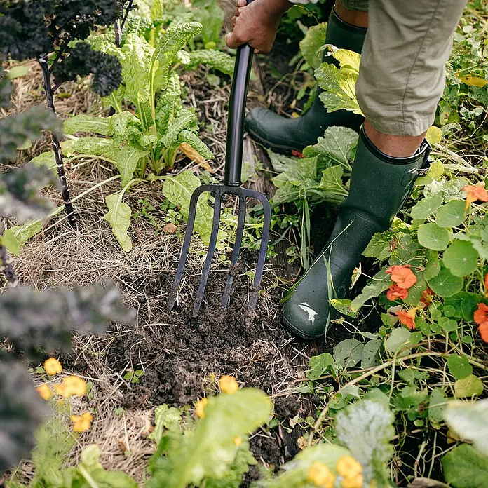 Fiskars Solid Spatengabel - Anzahl Zinken: 4, Langstiel - Nahaufnahme einer Person, die mit einer Grabegabel im Garten arbeitet. Die robuste Gabel erleichtert das Umgraben des Bodens.
