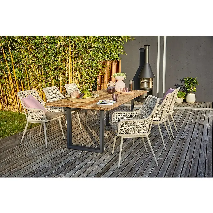 Sunfun Gartenmöbel-Set Zoe Dining - 8 -tlg., Baumkante/U-Gestell, Teak/Edelstahl/Kunststoffgeflecht, Teak/Grau - Eine Gartengarnitur mit einem Holztisch und sechs Korbstühlen auf einer hölzernen Terrasse, umgeben von Pflanzen.