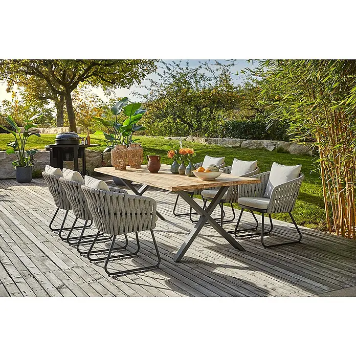 Sunfun Gartentisch - L x B x H: 220 x 100 x 75 cm, Teakholz/Edelstahl, Natur/Anthrazit, Baumkante/X-Fuß - Einladende Gartenszene mit einem Esstisch aus Holz und sechs eleganten Seilstühlen auf einer hölzernen Terrasse, umgeben von Grünpflanzen.
