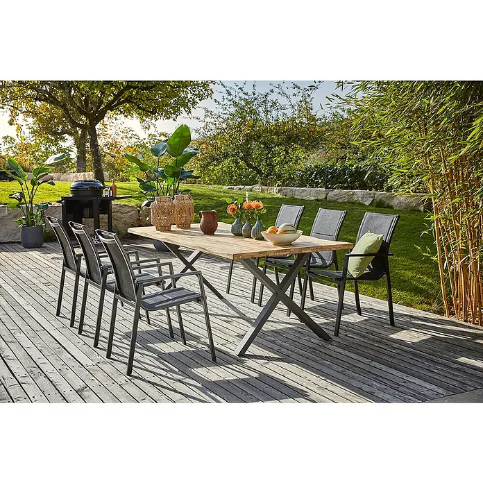 Sunfun Garten-Tischplatte220 x 100 cm, Teakholz, Baumkante - Ein Gartentisch mit sechs Stühlen auf einer Holzterrasse. Der Tisch ist aus Holz mit einem Metallgestell.