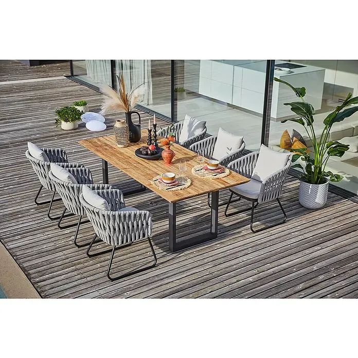 Sunfun Maja Gartenmöbel-Set - 8 -tlg., Teak/Edelstahl/Seilgeflecht, Teak/Grau/Beige, Schweizer-Kante/U-Gestell - Ein Gartentisch-Set mit sechs Stühlen auf einer Holzterrasse, dekoriert mit Pflanzen und Geschirr, ideal für Mahlzeiten im Freien.