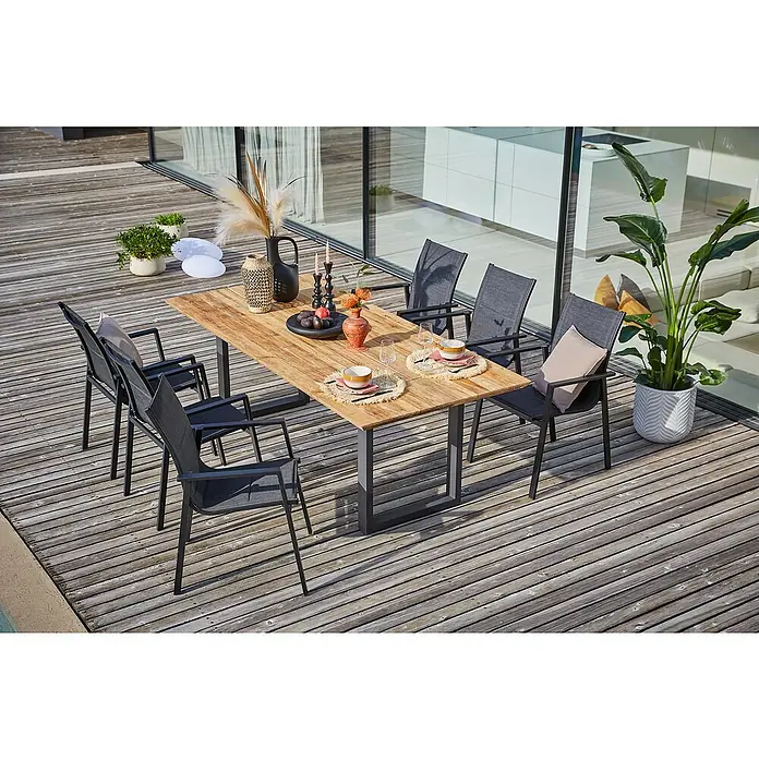 Sunfun Maja Gartenmöbel-Set - 8 -tlg., Schweizer-Kante/U-Gestell, Teak/Edelstahl/Textilen, Teak/Grau - Ein moderner Gartentisch mit sechs Stühlen auf einer Holzterrasse, dekoriert mit Pflanzen und Geschirr, bietet eine stilvolle Atmosphäre im Freien.