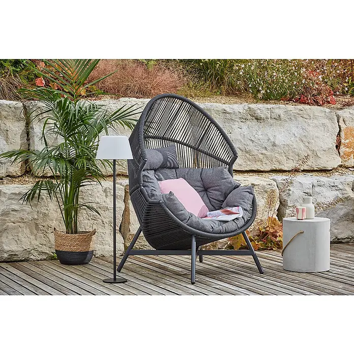 Loungesessel Ruhekokon - B x T x H: 100 x 98 x 142 cm, Metall, Kunststoffgeflecht, Schwarz - Ein stilvoller Hängekorbsessel mit grauen Polstern und einem rosa Kissen, ergänzt durch eine Stehlampe und einen Beistelltisch auf einer Holzterrasse.
