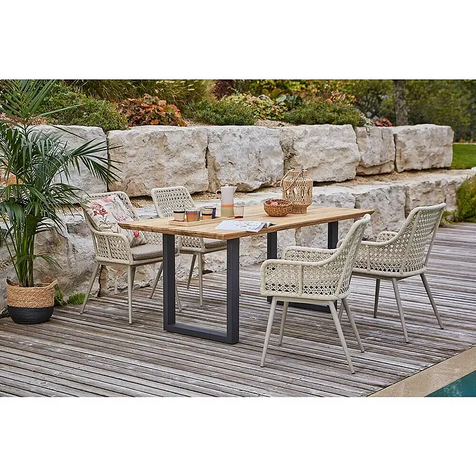 Sunfun Gartenmöbel-Set Zoe Dining - 6 -tlg., Schweizer-Kante/U-Gestell, Teak/Edelstahl/Aluminium/Kunststoffgeflecht, Teak/Grau/Sand - Gartenszene mit einem Teakholztisch mit Metallgestell und vier Outdoor-Stühlen mit Flechtmuster auf einer Holzterrasse.