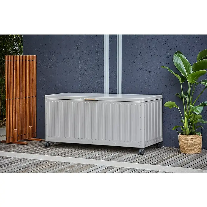 Gartenbox - 164 x 74 x 70 cm, Stahl, Hellgrau - Eine graue Aufbewahrungsbox mit Rädern steht auf einer Terrasse, daneben ein Holzschutzzaun und eine Pflanze im Korb.
