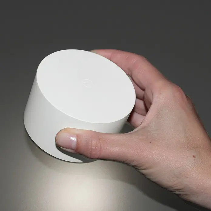 FHL easy Magnetic Akku-Wandleuchte - 9,5 x 8 x 4,5 cm, Weiß, Mehrfarbig, 2 W, IP20 - Eine Hand hält einen zylindrischen, weißen Google Nest Wifi Router vor einem neutralen Hintergrund. Das Gerät wirkt schlicht und modern.