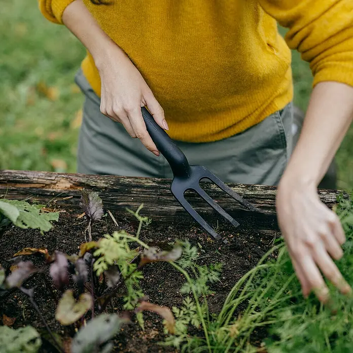 Fiskars Solid Hand-Kleinrechen - 27,7 cm - Nahaufnahme einer Person, die einen Fiskars Handgrubber in einem Gartenbeet benutzt, ideal für die Gartenarbeit.