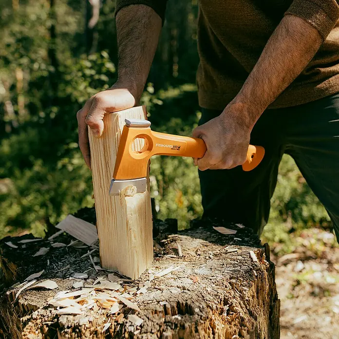 Fiskars X-series Universalaxt X13 - Länge: 33,2 cm - Nahaufnahme einer Person, die mit einer Fiskars X13 Spaltaxt Holz spaltet, wobei der Fokus auf der orangenen Axt liegt.