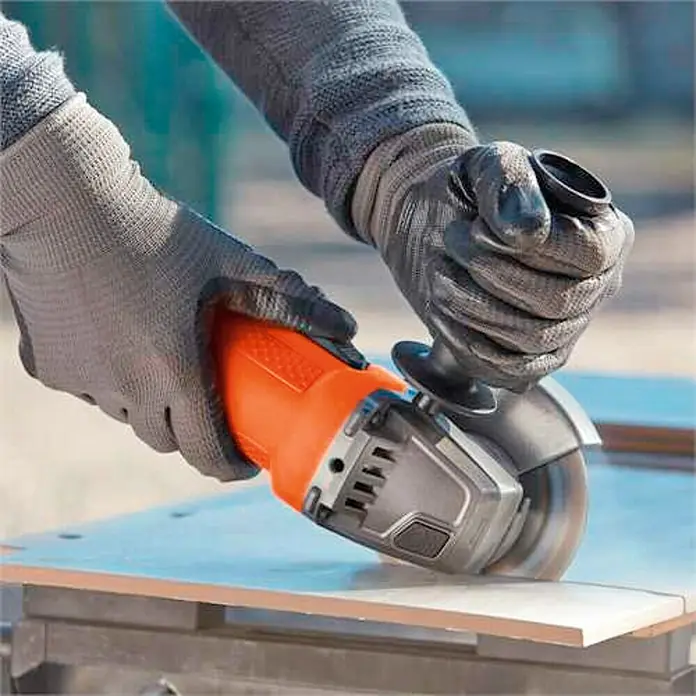 Black+Decker Amoladora angular eléctrica BEG110 - 750 W, 115 mm - Una persona usa una amoladora angular para cortar una baldosa. La amoladora angular es naranja y negra y se está operando con guantes.