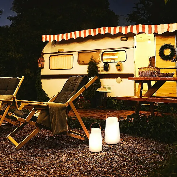 FHL easy Akku-Tischleuchte COLLGAR - 0,5 W, L x B x H: 12,5 x 12,5 x 21 cm, Weiß, RGB - Stimmungsvolle Szene mit zwei tragbaren Laternen, die eine gemütliche Atmosphäre vor einem Wohnwagen schaffen.