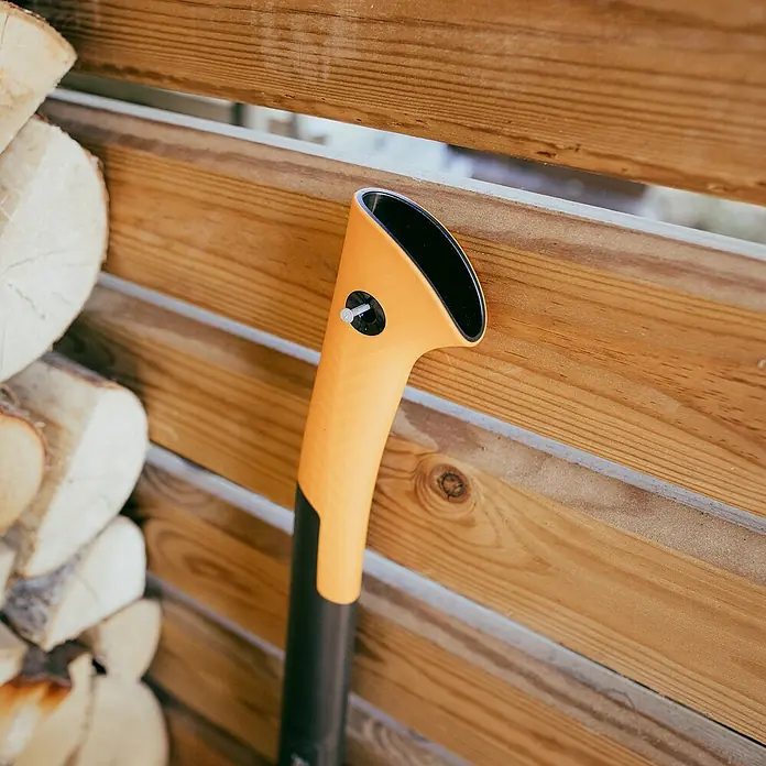 Fiskars X-series Universalaxt X18Länge: 44,5 cm - Nahaufnahme einer Fiskars Spaltaxt an einer Holzwand, ideal zum Holzspalten. Das Werkzeug ist robust und effizient.