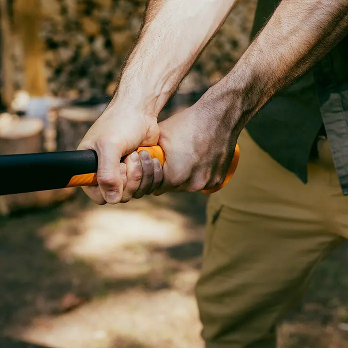 Fiskars X-series Spaltaxt X32 - Länge: 81,5 cm - Nahaufnahme von Händen, die einen Axtgriff halten, der die Kraft und Präzision des Werkzeugs für Holzarbeiten hervorhebt.