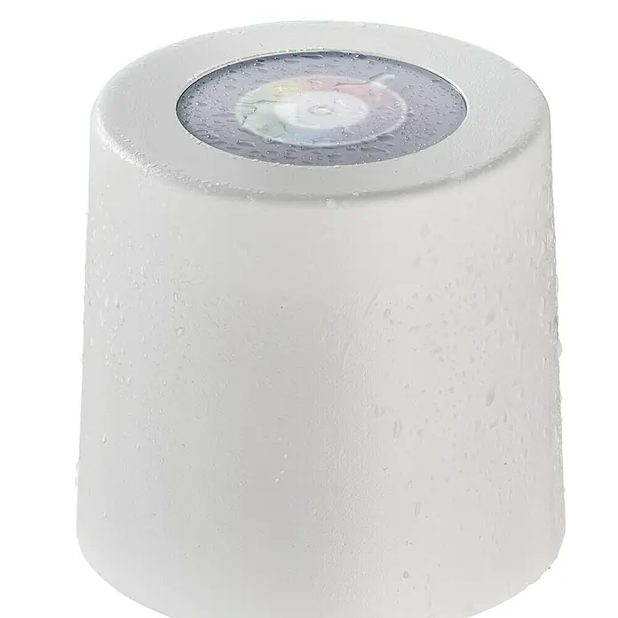 SCHÖNER WOHNEN-Kollektion Akku-Tischleuchte SUN - 2 W, L x B x H: 12 x 12 x 38 cm, Sandweiß, RGB - Das Foto zeigt eine weiße runde Lampe, die mit Wassertropfen bedeckt ist. Das Licht ist in verschiedenen Farben im Zentrum sichtbar.