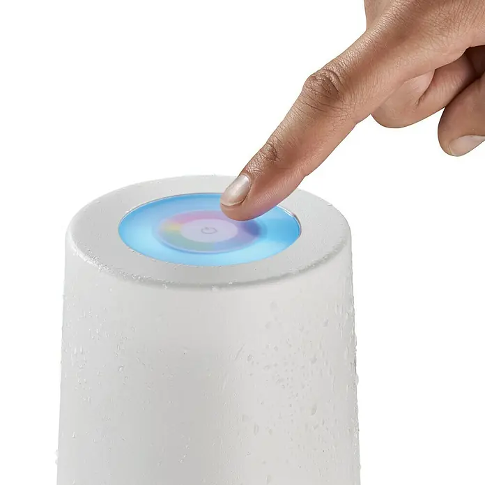 SCHÖNER WOHNEN-Kollektion Akku-Tischleuchte SUN - 2 W, L x B x H: 12 x 12 x 38 cm, Sandweiß, RGB - Ein Finger berührt die Oberseite einer weißen Tischleuchte mit Farbwechsel. Moderne, minimalistische Beleuchtung für gemütliche Atmosphäre.