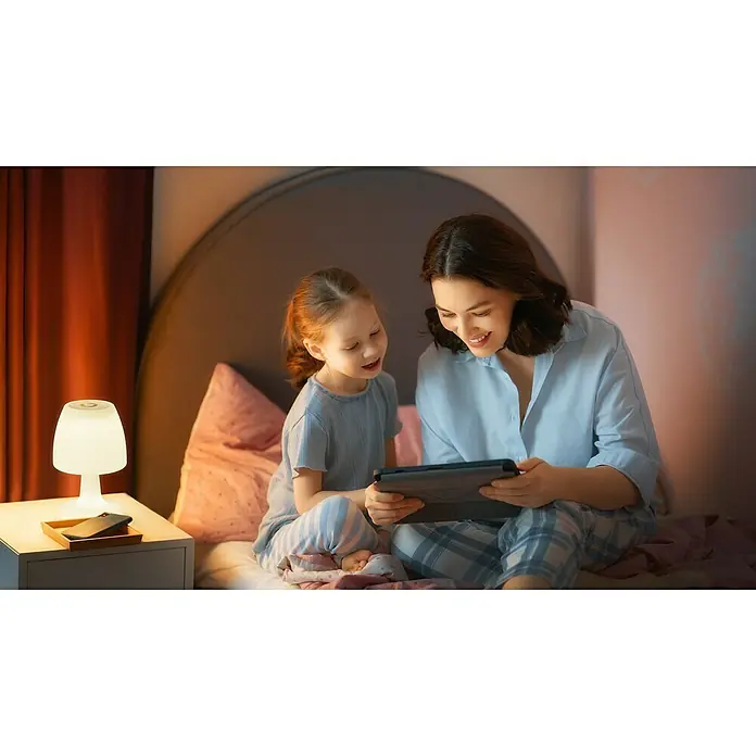 FHL easy Akku-Tischleuchte BARLETTA - 2 W, L x B x H: 16 x 16 x 26 cm, Weiß, RGB - Mutter und Tochter schauen sich ein Tablet im Bett an, beleuchtet von einer Tischlampe. Sie genießen die gemeinsame Zeit mit dem Gerät.