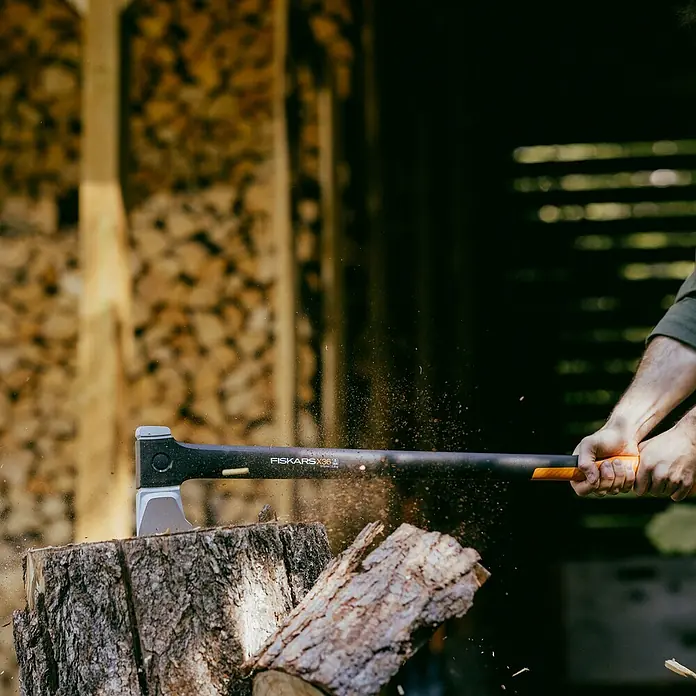 Fiskars X-series Spaltaxt X36 L - Länge: 91,5 cm - Eine Axt der Marke Fiskars spaltet einen Baumstamm, Holzsplitter fliegen umher. Das Werkzeug ist robust und ideal für die Holzbearbeitung.