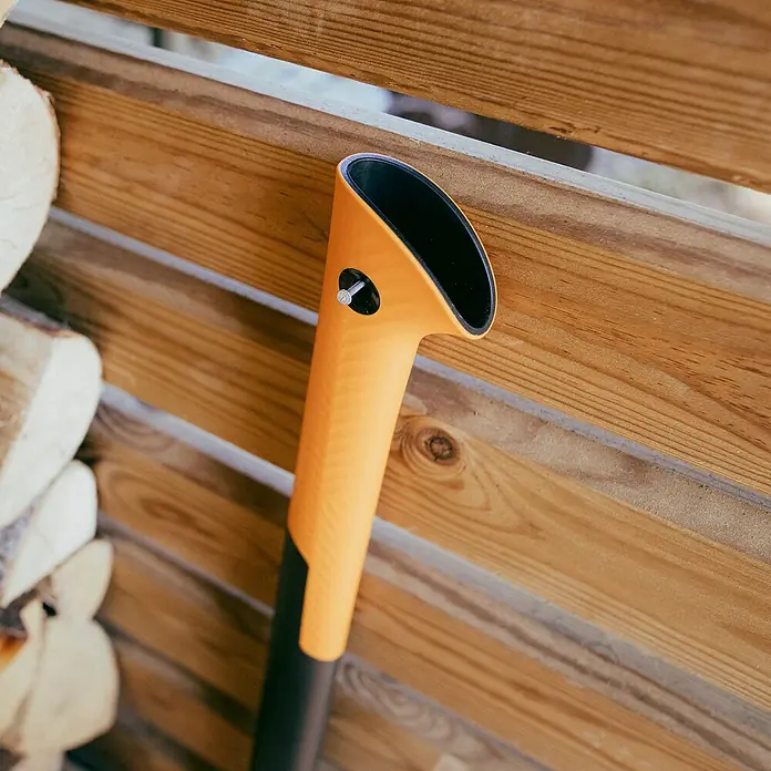 Fiskars X-series Spaltaxt X36 L - Länge: 91,5 cm - Nahaufnahme einer Holzspaltaxt mit orangem Griff, die an einer Holzwand befestigt ist, ideal für die Brennholzbearbeitung.