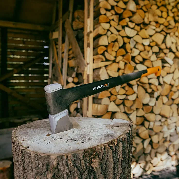 Fiskars X-series Spaltaxt X36 L - Länge: 91,5 cm - Nahaufnahme einer Axt der Marke Fiskars auf einem Holzscheit, im Hintergrund ein Holzstapel.