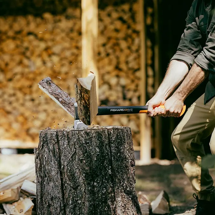 Fiskars X-series Spaltaxt X24 M - Länge: 60 cm - Ein Mann spaltet mit einer Fiskars X24M Axt Holz auf einem Hackklotz. Die Axt ist im Einsatz und das Holz wird gespalten.