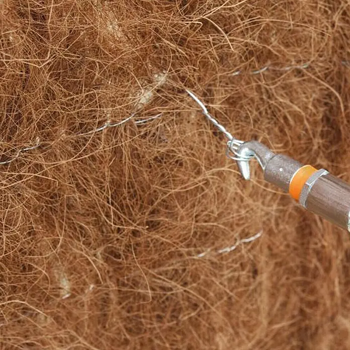 Alambre galvanizado - Ø x L: 0,7 mm x 50 m - Primer plano de un atador de nudos utilizado para torcer y asegurar alambres sobre un fondo marrón y fibroso.