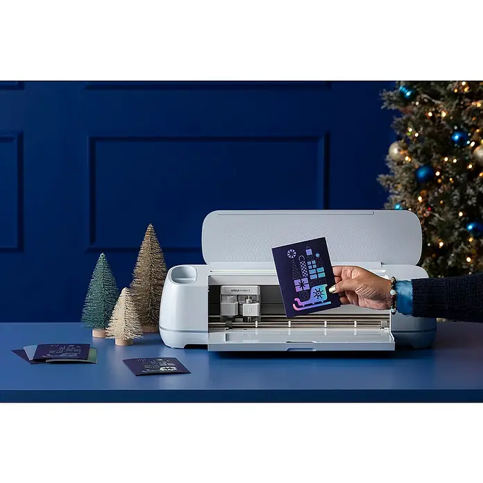 Cricut Maker Schneideplotter Maker 3 - Blau, Bluetooth, Schnittbreite: 29,7 cm, Schnittlänge: 3,6 m - Eine Cricut Maker 3 Schneidemaschine mit einer festlichen Weihnachtskarte im Vordergrund, die ein weihnachtliches Design zeigt.