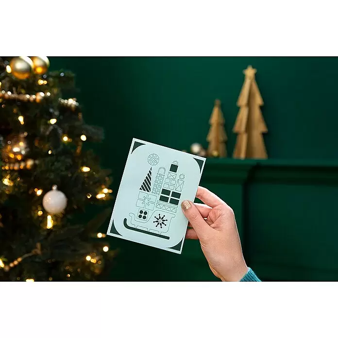Cricut Joy Schneideplotter Starter Bundle - Türkis/Weiß, Bluetooth, Schnittbreite: 10,4 cm, Schnittlänge: 1,2 m - Hand hält eine hellgrüne Weihnachtskarte mit dunkelgrünem Schlitten- und Geschenkmotiv in festlicher Umgebung.