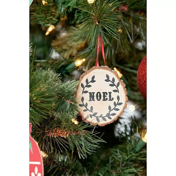 Cricut Joy Schneideplotter Smarte Schneide- und Zeichenmaschine - Türkis/Weiß, Bluetooth, Schnittbreite: 10,4 cm, Schnittlänge: 1,2 m - Rundes Holzornament "NOEL" mit schwarzem Text und rotem Band an einem Weihnachtsbaum.