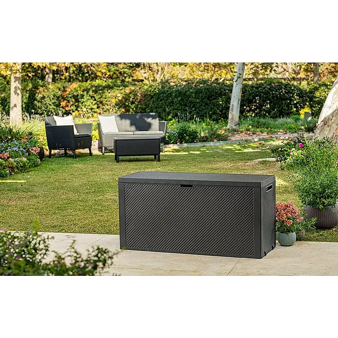 Keter Arcón para cojines de exterior Emily - 117,8 x 44,6 x 58 cm, Plástico, Gris - Una caja de almacenamiento de jardín negra en un patio, rodeada de un jardín bien cuidado. La caja ofrece almacenamiento para suministros.