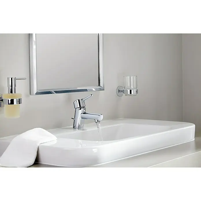 Grohe Essentials Seifenspender - Mit Halterung, Chrom, Glänzend - Ein modernes Badezimmerwaschbecken mit einem glänzenden Wasserhahn, einem Seifenspender und einem Spiegel an der Wand.