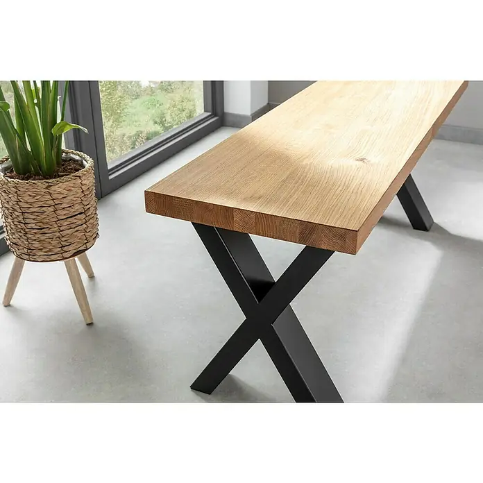 Pur Iternal Select Tischbein - 330 x 100 x 390 mm, Schwarz, X-Form - Detailaufnahme einer modernen Sitzbank mit einer hellen Holzplatte und schwarzen X-förmigen Metallbeinen, neben einer Zimmerpflanze.