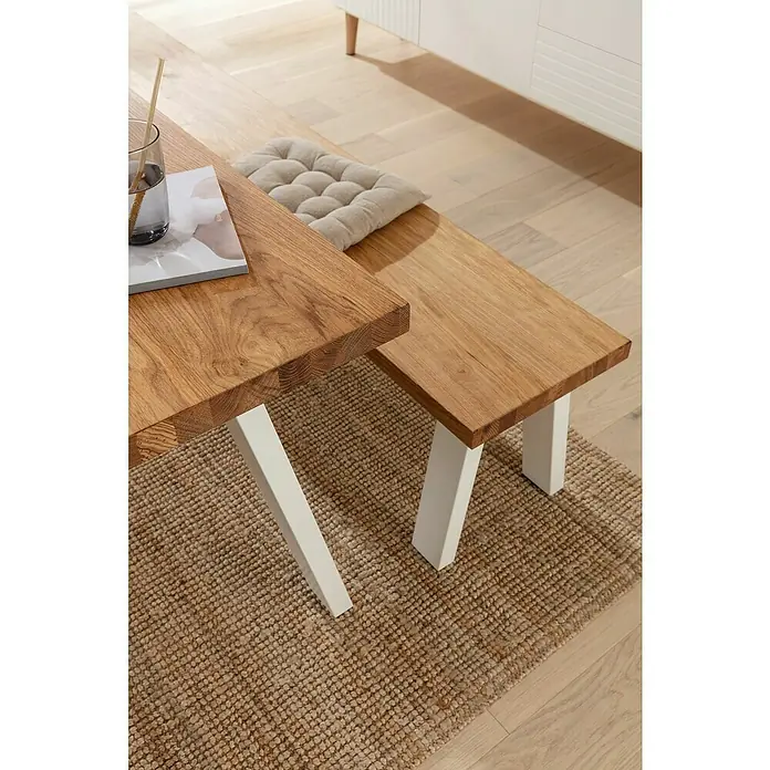 Pur Iternal Select Tischbein - 330 x 100 x 390 mm, Weiß, U-Form - Nahaufnahme eines robusten Esstisches mit Holzbänken und weißen Beinen, die auf einem rustikalen, geflochtenen Teppich stehen.