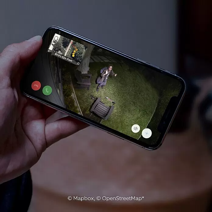 Ring Cámara de vigilancia Ring Spotlight Cam Pro Wired - Blanco, Ángulo de detección: 140 °, Funcionamiento en red - Smartphone mostrando una cámara de seguridad en vivo de una persona en un jardín de noche, con mapa y opciones de llamada.