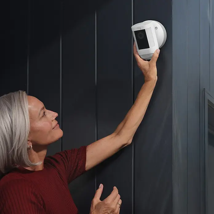 Ring Überwachungskamera Spotlight Cam Pro Wired - Weiß, Auflösung: 1.080 Pixel (Full HD), Festverdrahtet - Frau installiert eine Ring Spotlight Cam zur Überwachung. Die kabellose Kamera bietet Sicherheit und Komfort für jedes Zuhause.