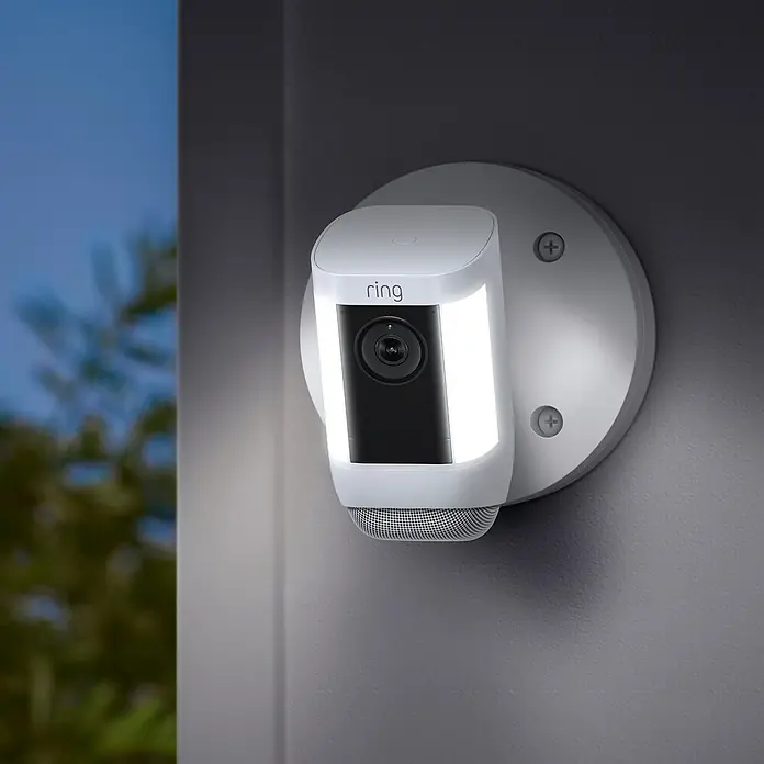 Ring Überwachungskamera Spotlight Cam Pro Wired - Weiß, Auflösung: 1.080 Pixel (Full HD), Festverdrahtet - Ring Spotlight Cam im Außenbereich. Die Überwachungskamera ist mit Lichtern ausgestattet und auf einer Wand montiert.